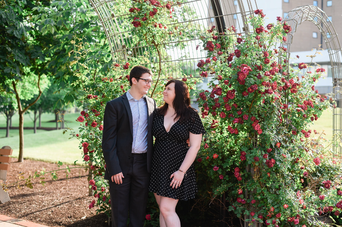 Couple smiles at each other in front of a rose bush during their Highbanks Metro Park Engagement Session